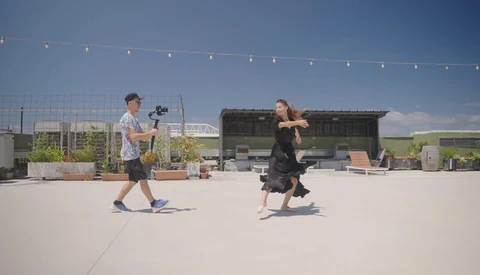 Cinematographer operating a camera on a rooftop while a woman in black performs movement for filming.