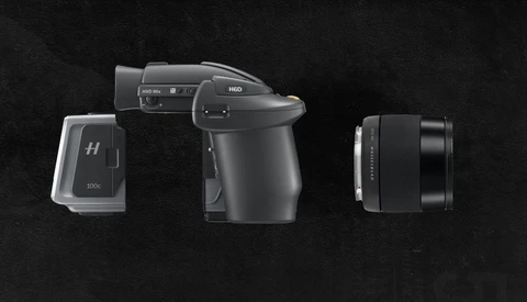 Three professional camera components arranged against a dark background: a medium format camera body with viewfinder, a battery or power module, and an interchangeable lens.
