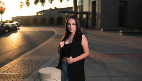Woman in black sleeveless vest standing on a paved plaza during golden hour lighting.