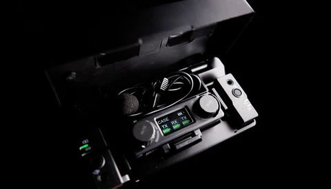 Professional audio recorder with microphone and cables displayed in an open carrying case against black background.