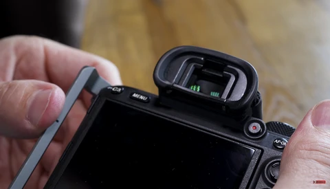 Close-up of a mirrorless camera's electronic viewfinder and top controls held in hands.