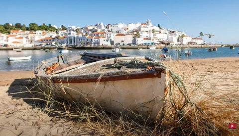 Weathered wooden fishing boat beached on sand with Mediterranean coastal town in background.