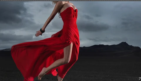 Woman in flowing red dress against dark mountainous landscape under stormy sky.