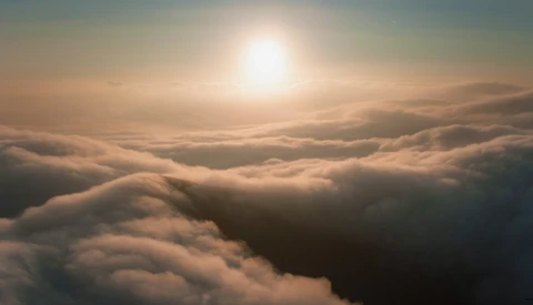 Sun rising above a thick blanket of clouds with dramatic golden light illuminating the cloud formations.