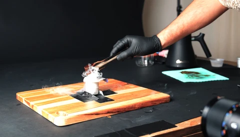 Hands in black gloves applying white substance to orange and white striped wooden board during demonstration.