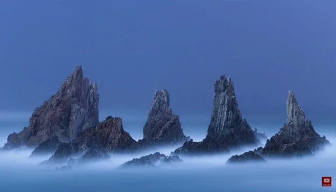 Jagged rock formations rising through heavy mist against a clear blue sky.