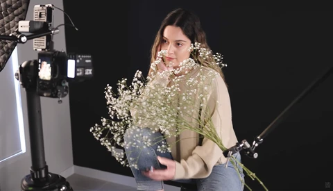 Woman holding baby's breath flowers in studio with professional lighting setup visible.