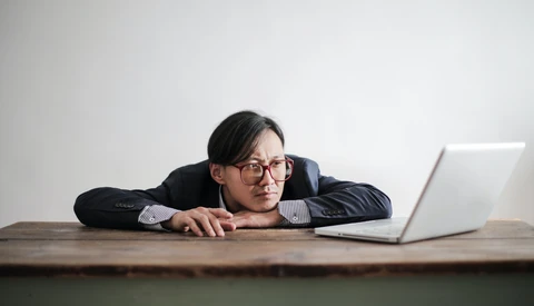 Man in business casual attire leaning on desk toward laptop with relaxed posture.