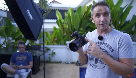 Videographer holding a professional camera during an outdoor shoot in a courtyard setting with studio lighting.