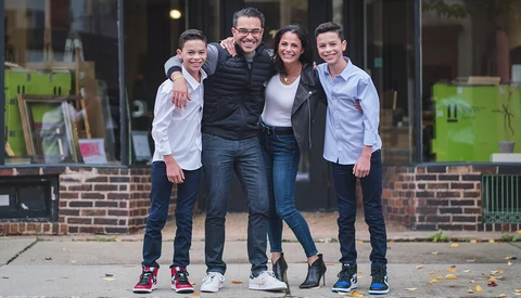 Five young people smiling at the camera while standing together on a brick-lined urban street.