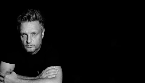 Black and white portrait of a man with styled hair against a dark background.