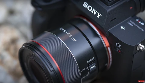 Sony mirrorless camera with red-accented lens mounted, showing camera body and lens detail in close-up.