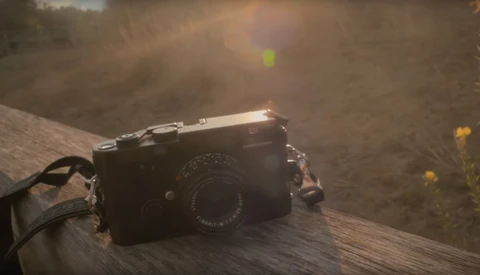Rangefinder camera with leather strap resting on weathered wood surface in natural outdoor setting.
