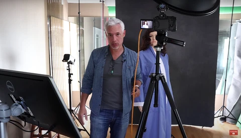Two people in a professional studio setup with lighting equipment and camera on tripod.
