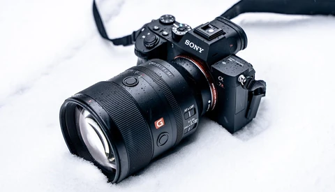 Sony mirrorless camera with telephoto lens mounted, positioned on white snowy surface.