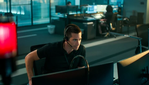 Male content creator wearing headphones while working at a computer setup in a modern office environment with red accent lighting.