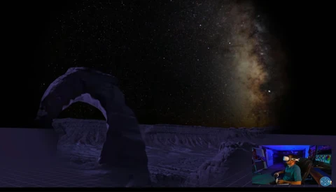 Night sky photograph showing the Milky Way above an illuminated dome structure with a person visible in the foreground.