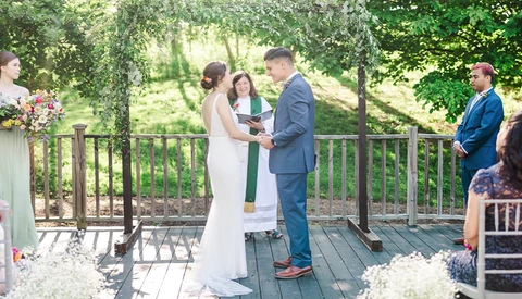Bride and groom exchange vows during outdoor wedding ceremony on wooden deck.