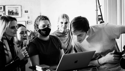 Five people gathered around a laptop screen in a bright studio space, examining content together.