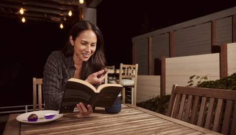 Woman reading a book at a wooden table in a studio setting with warm overhead lighting.