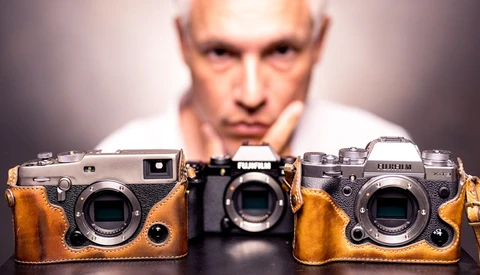 Three rangefinder cameras with brown leather cases displayed in front of a blurred male figure.