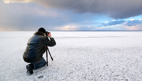 Photographer crouching on a salt flat, composing a shot with a tripod-mounted camera during golden hour.
