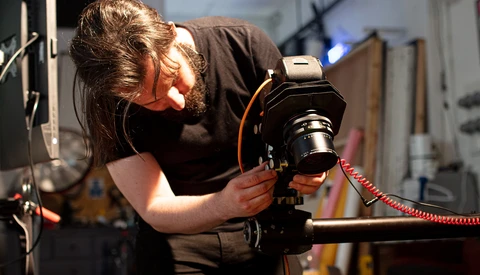 Photographer operating a camera mounted on a tripod with a red coiled cable attachment.