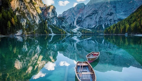 Two wooden rowboats on glassy turquoise water surrounded by steep rocky mountains and evergreen forest.