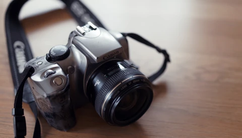 Silver film SLR camera with black lens and shoulder strap on wooden surface.