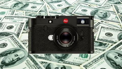 Leica M rangefinder camera with black leather body positioned on a background of US hundred-dollar bills.