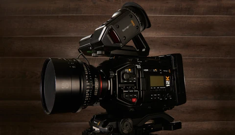 Professional cinema camera with prime lens and top-mounted monitor on wooden surface.
