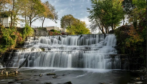 Multi-tiered waterfall cascading through forested landscape with smooth water flow effect.