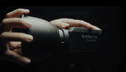 Hands holding a Nanlite Forza 50 LED light against a black background.