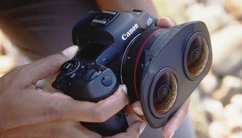 Canon camera with dual-lens attachment held in someone's hands alongside a wireless controller.