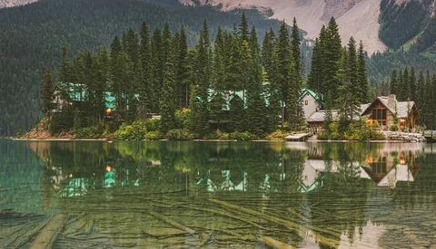 Lakeside cabins nestled among dense evergreen forest with mirror-like water reflection.