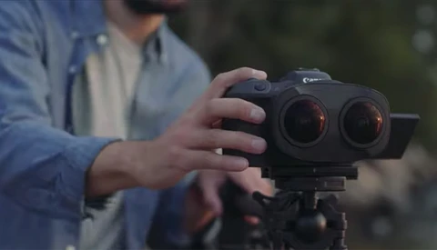 Photographer holding a dual-lens camera rig on a tripod during outdoor filming.