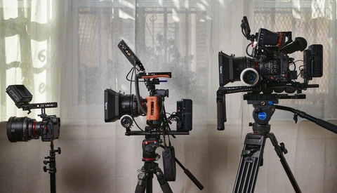 Three cinema cameras mounted on tripods with microphones and support rigs in a studio setting.