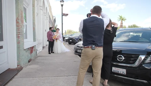 Wedding photographer capturing a bride and groom on a residential street lined with parked cars.