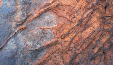 Aerial view of geological formations showing rust-colored striations and erosion patterns on rocky terrain.
