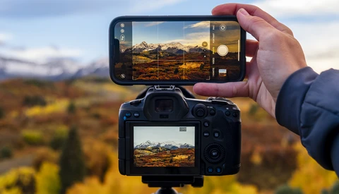 Smartphone and DSLR camera displaying the same mountain landscape scene during golden hour.