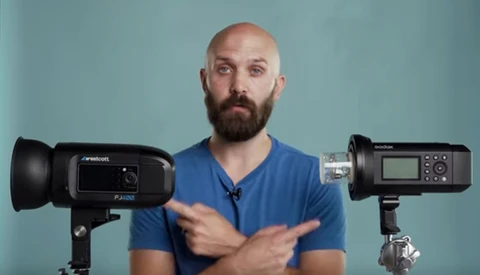 Man in blue shirt comparing two professional LED light fixtures against a teal background.
