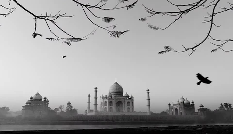 Silhouetted domes and minarets of a grand monument across a misty river, framed by bare tree branches overhead.