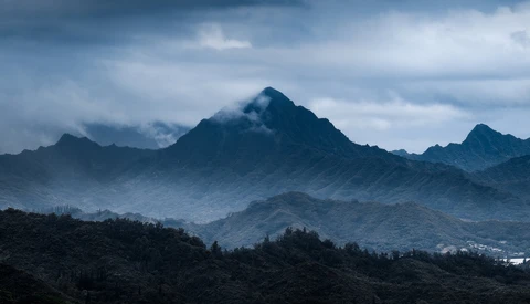 Layered mountain peaks shrouded in mist and clouds under a dramatic blue-gray sky.
