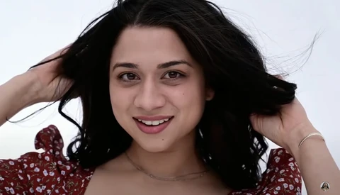 Young woman with long black hair smiling at camera against white background.