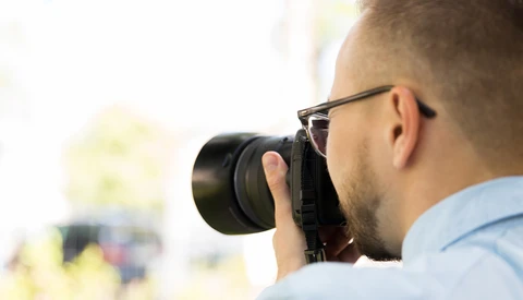 Photographer wearing glasses holding a camera to his face while looking through the viewfinder.