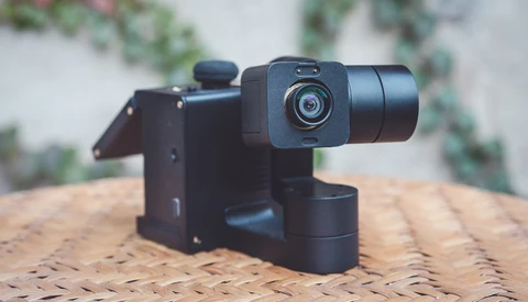 Black motorized gimbal with compact camera mounted on woven surface outdoors.