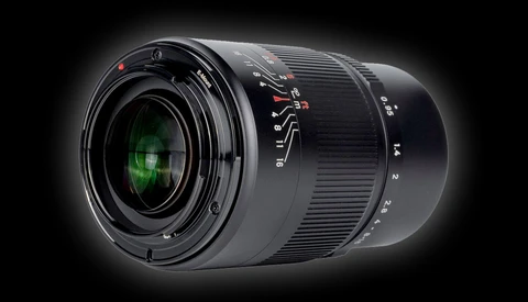 Black camera lens with green glass elements visible through the front, shot against a dark background with dramatic lighting.