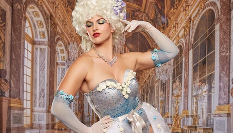 Woman in elaborate white costume with jeweled corset poses in ornate baroque interior.