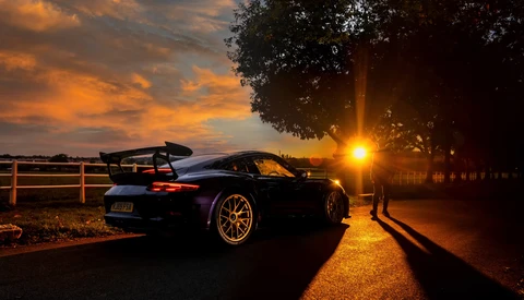 Black sports car with open trunk and gold wheels photographed at golden hour sunset.