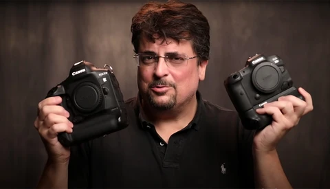 Photographer holding two professional DSLR camera bodies side by side for comparison.